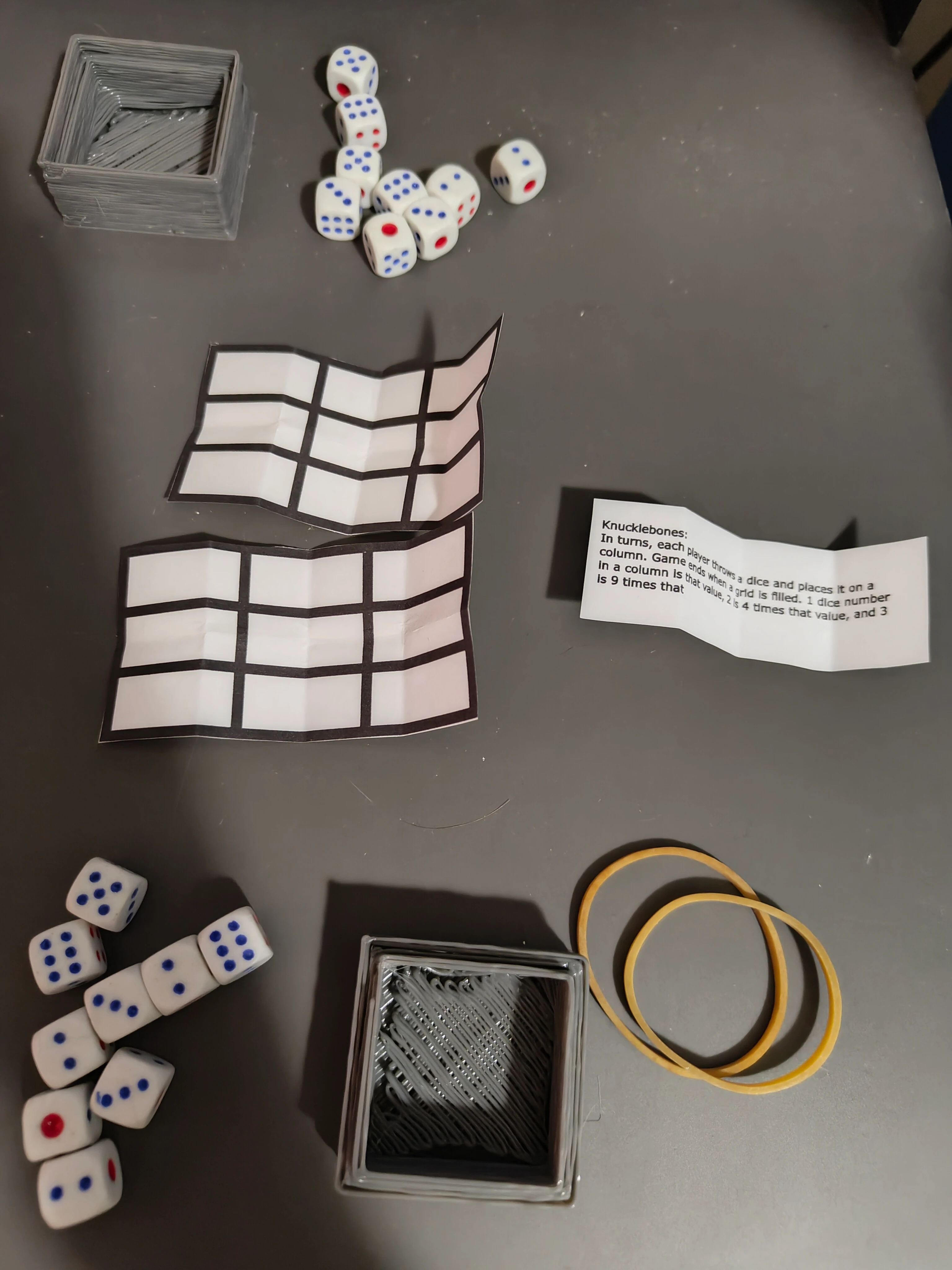 The dice, box, rubber bands, grids and instructions set on a table